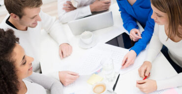 View from above of a motivated young business team holding a meeting sitting together around a table littered with paperwork